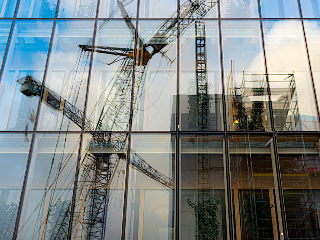 Reflection on Mirrored Windows of Crane Lifting Construction Materials Up To The Top of a High-rise Construction Site