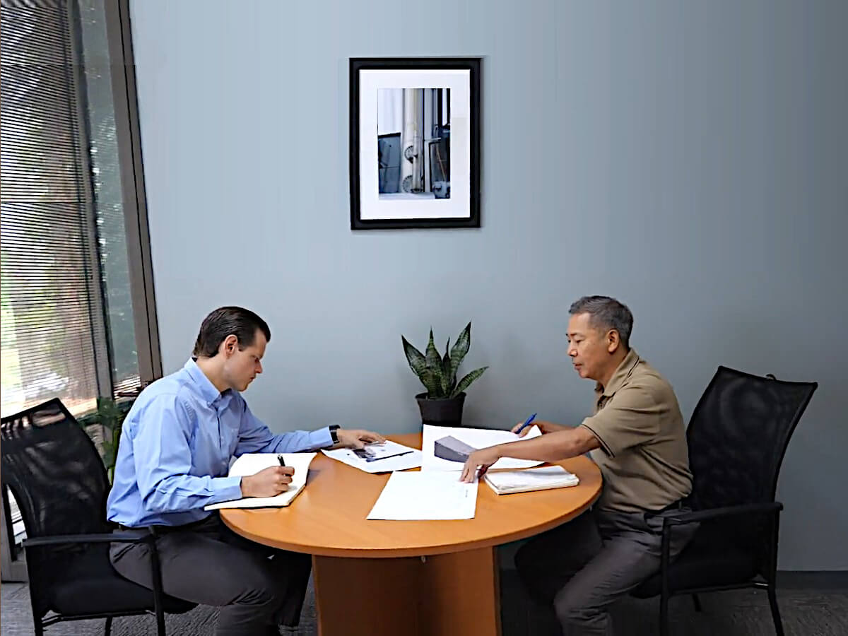 Two Members of Pollution Systems’ Engineering Group sit at a round brown table and discuss the Best System Choice for a Customer’s Application Process while looking at drawings