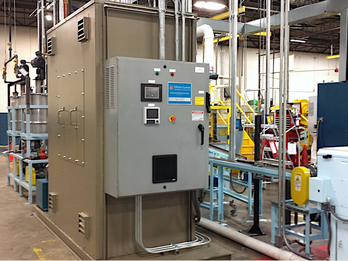 Electric Catalytic Oxidizer Installed Indoors Treats Heptane VOC for a Metal Packaging Facility. The Green Electric Catox is against a white wall with dark ceiling and surrounded by Silver Pipes and Yellow, Blue, Red and White Equipment.