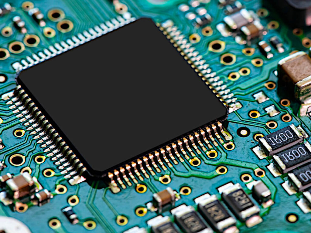Close-up view of Turquoise Colored Microelectronic Circuit Board with a Large Square Black Semiconductor and smaller Copper, black and silver microchips and terminals