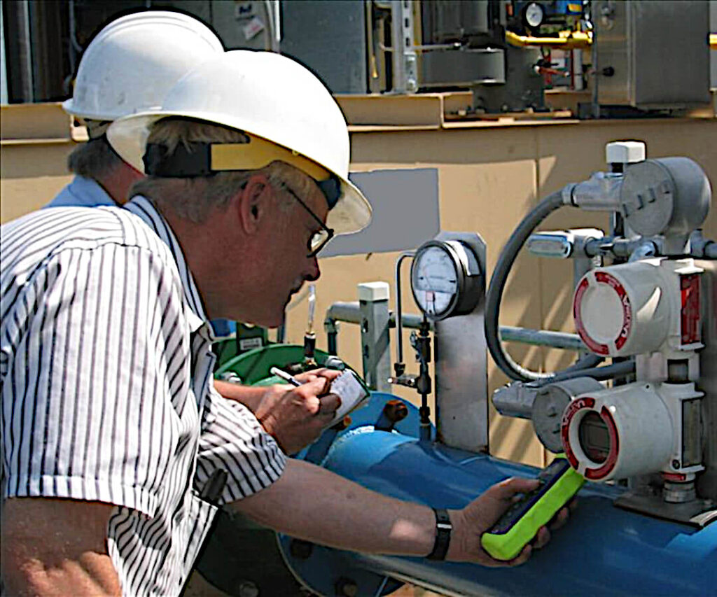 Two Project Engineers with White Hard Hats Test Pressure of a System using a Green Pressure Gauge Gadget.