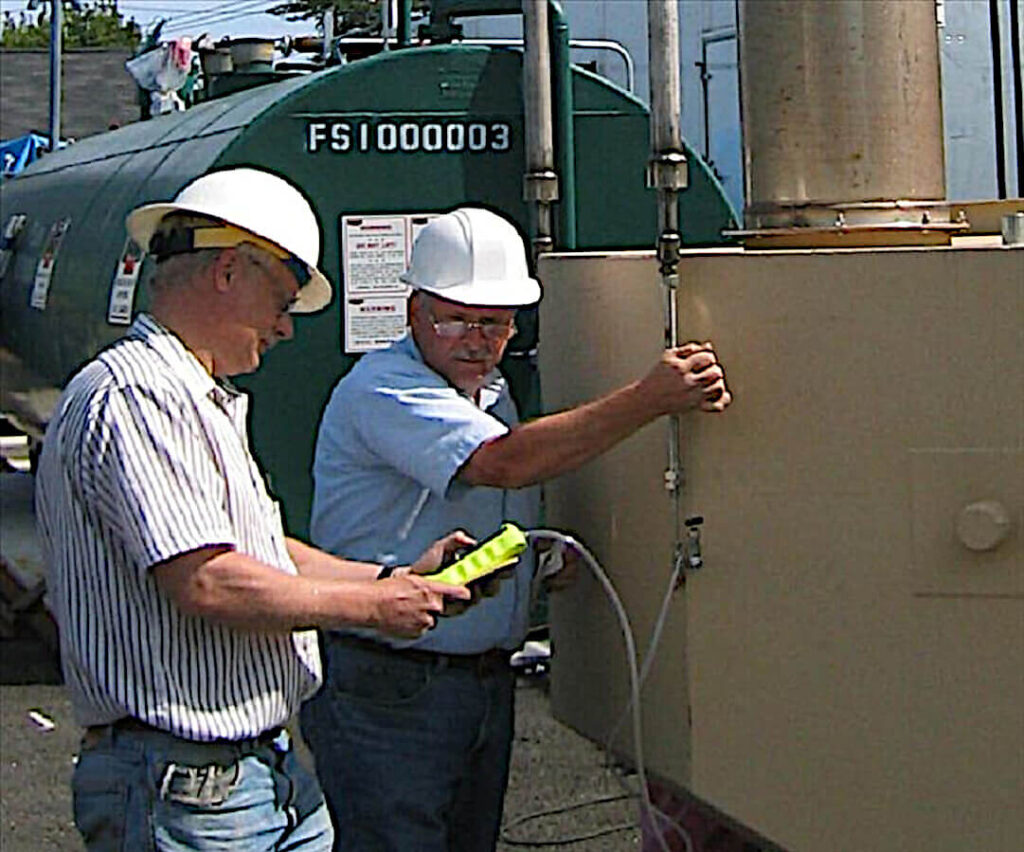 Two Male Project Engineers with White Hard Hats and Jeans Perform An Evaluation of System Functionality During Start-up and commissioning of a Green and Tan Air Pollution Control Unit