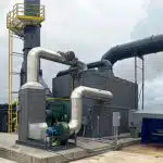 Box-shaped gray machinery (concentratror) on a cement platform outside of an industrial plant. An oxidizer system is behind and to the left of the concentrator.
