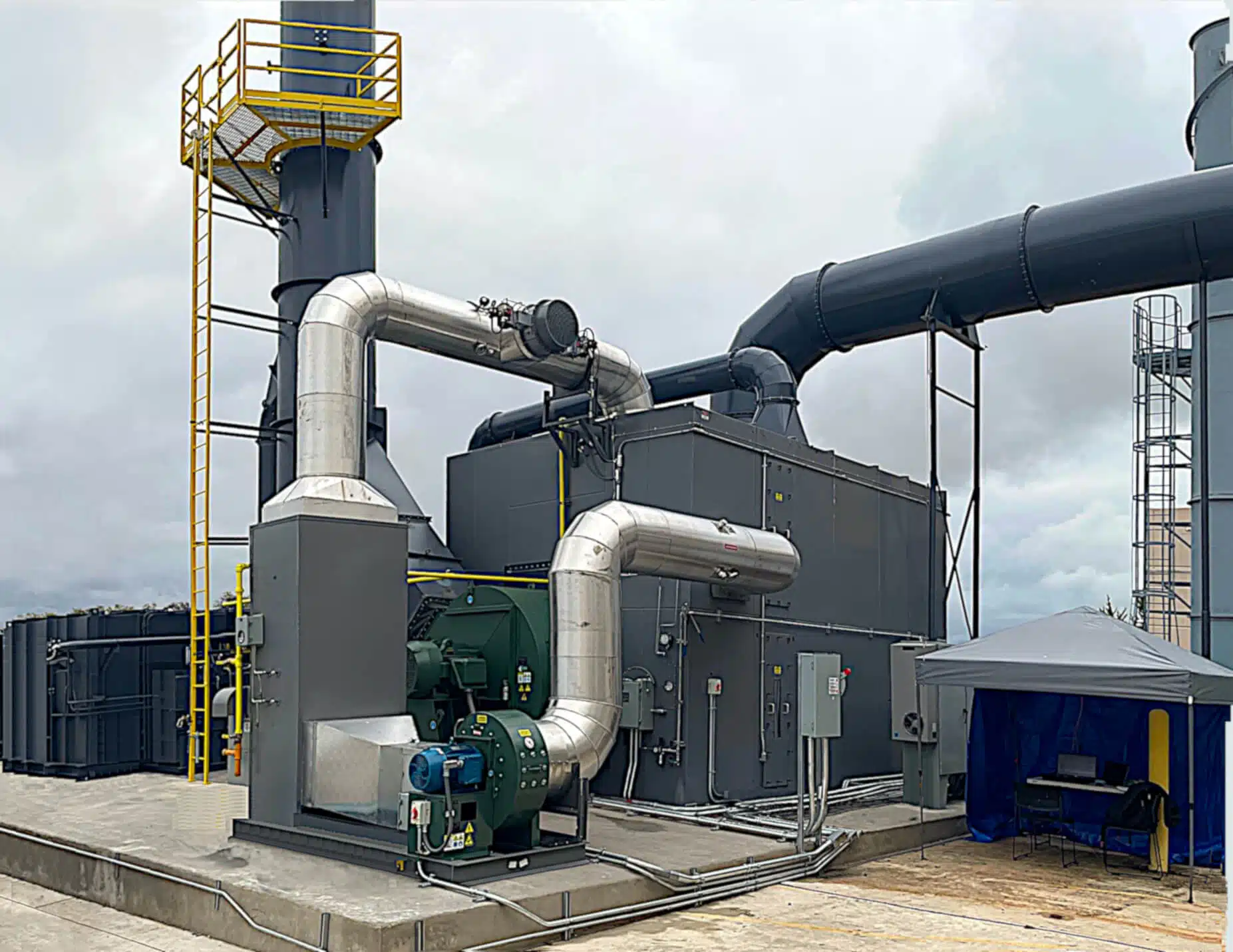 Box-shaped gray machinery (concentratror) on a cement platform outside of an industrial plant. An oxidizer system is behind and to the left of the concentrator.